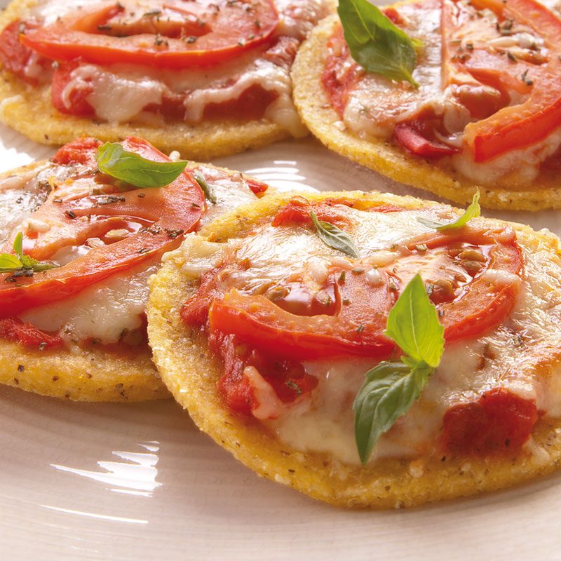 Arepas de maíz de trigo con tomate, queso y hojas de albahaca sobre un plato blanco.