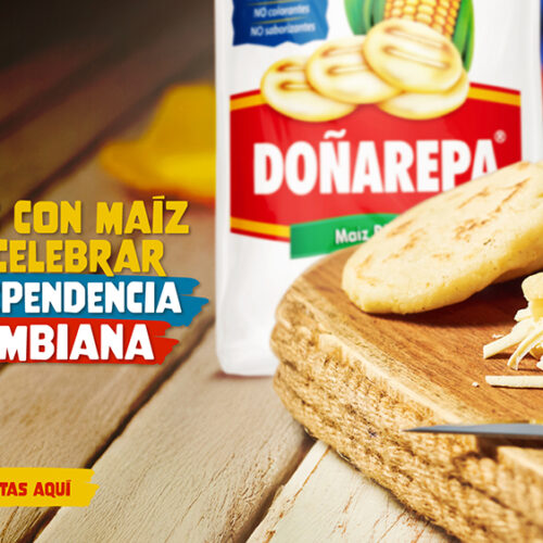 Vista de varias arepas de maíz rellenas con queso rallado sobre una tabla de madera. Al fondo, una tela de colores y contenedores con especias.